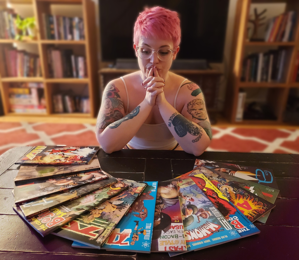 A photo of Chloe, who has pink cropped hair and tattoos, staring at a coffee table full of A1 comics.